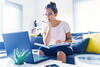 a woman on a couch with a book in her lap looking at her laptop on the coffee table